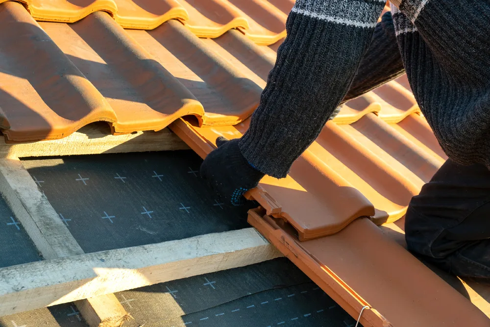 Closeup of worker hands installing yellow ceramic roofing tiles