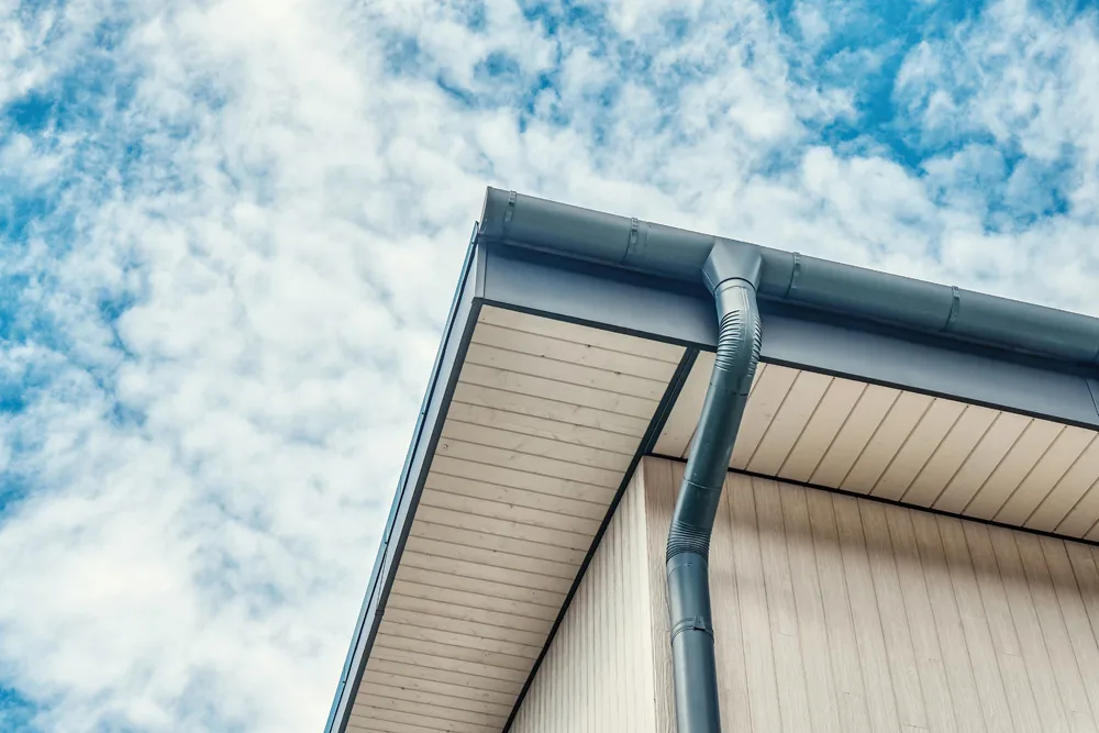 Contemporary grey metal rainwater downpipe installed on roof of new building on cloudy day close up