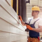 Handsome young man builder installing exterior wood siding